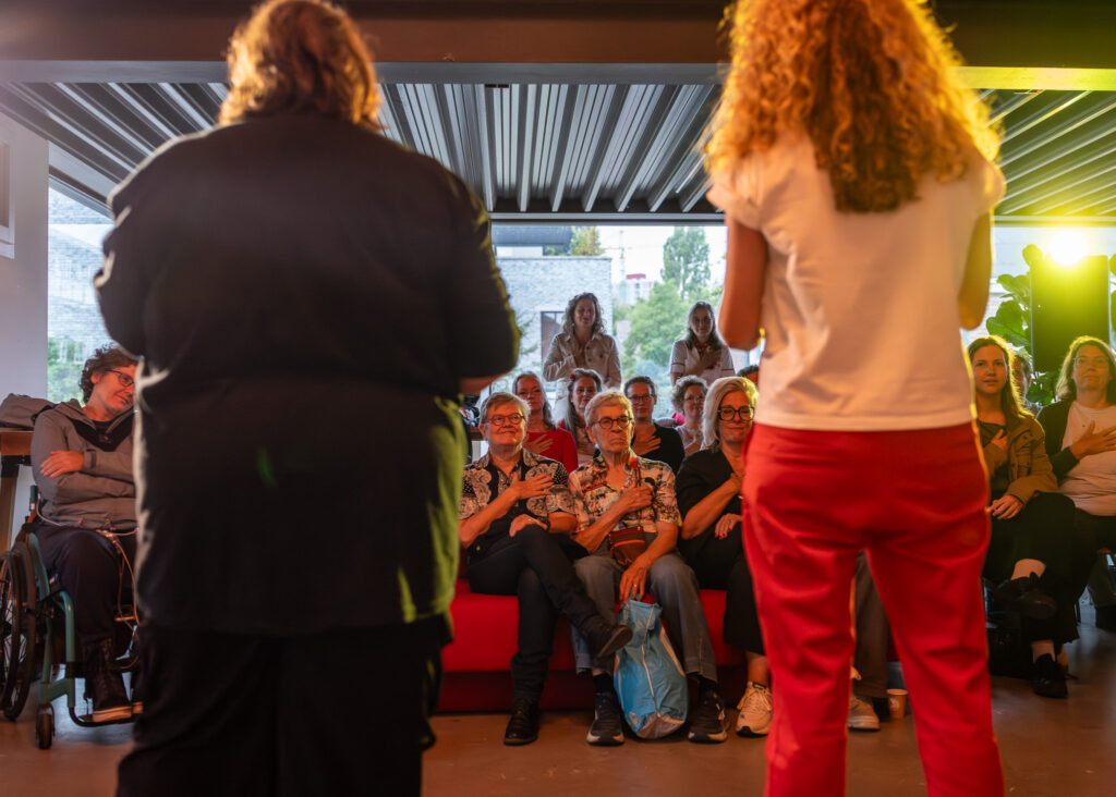 Inge en Wendie zie je op de rug en tussen hun door zie je een deel van het publiek